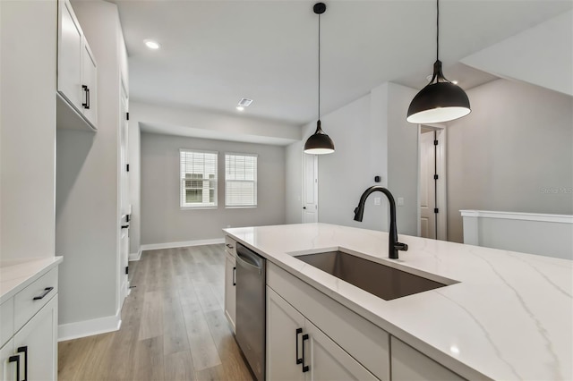 kitchen with light stone countertops, light wood-type flooring, stainless steel dishwasher, sink, and white cabinetry