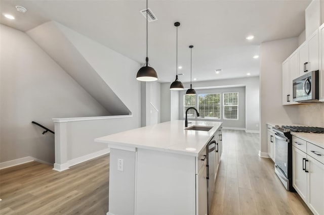 kitchen with pendant lighting, a center island with sink, sink, appliances with stainless steel finishes, and white cabinetry