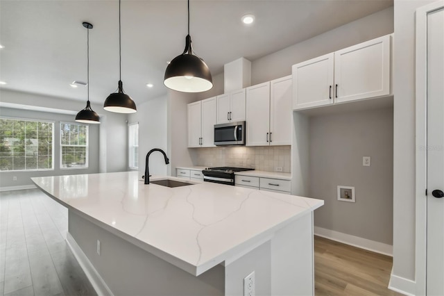 kitchen featuring a kitchen island with sink, sink, light stone countertops, appliances with stainless steel finishes, and decorative light fixtures