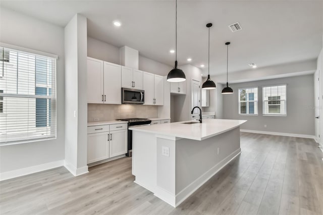 kitchen with a wealth of natural light, a kitchen island with sink, sink, and appliances with stainless steel finishes