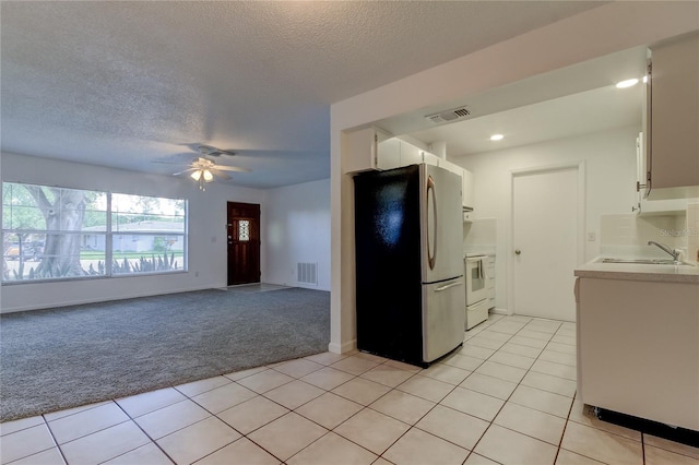 kitchen with sink, stainless steel fridge, light colored carpet, white cabinetry, and ceiling fan