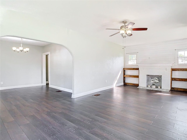 unfurnished living room with ceiling fan with notable chandelier, dark wood-type flooring, and a fireplace