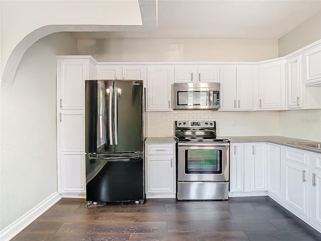 kitchen with white cabinets, light stone counters, appliances with stainless steel finishes, and dark hardwood / wood-style flooring