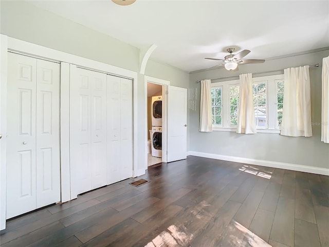 unfurnished bedroom with stacked washer / dryer, two closets, dark hardwood / wood-style flooring, and ceiling fan