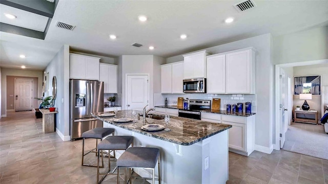 kitchen with white cabinets, sink, a kitchen island with sink, stainless steel appliances, and dark stone countertops