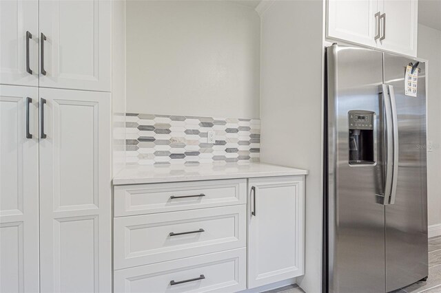 kitchen with light stone counters, stainless steel fridge with ice dispenser, and white cabinetry