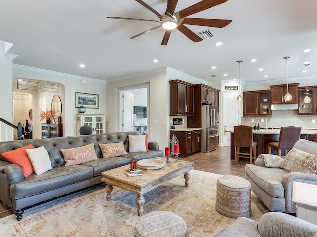 living room featuring wood-type flooring, ceiling fan, sink, and crown molding