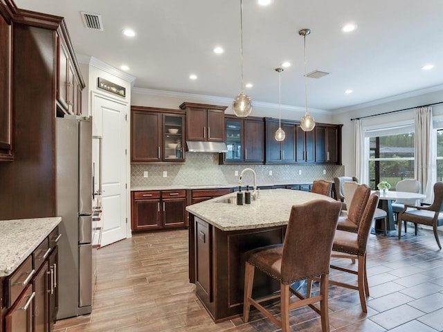 kitchen featuring stainless steel fridge, light stone counters, hanging light fixtures, and sink