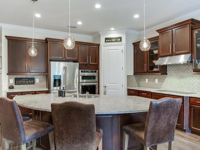 kitchen with decorative light fixtures, a kitchen island with sink, stainless steel appliances, and a kitchen breakfast bar