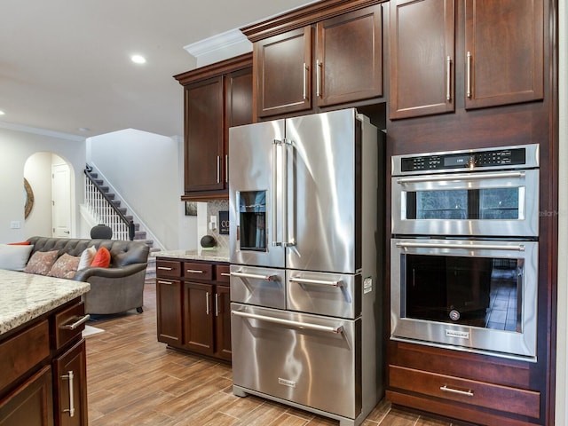 kitchen with dark brown cabinets, light stone counters, light hardwood / wood-style floors, stainless steel appliances, and crown molding