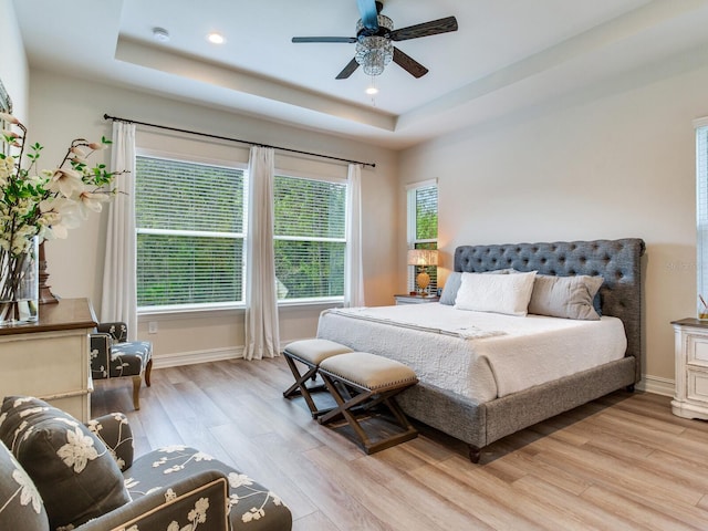 bedroom with light hardwood / wood-style flooring, a tray ceiling, and ceiling fan