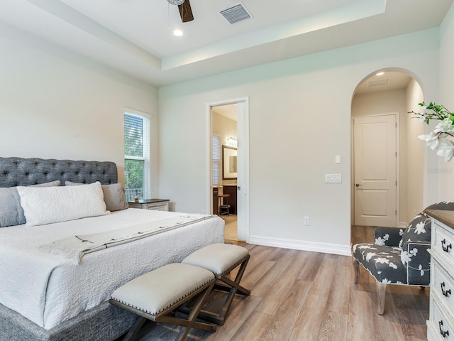 bedroom featuring ceiling fan, light hardwood / wood-style floors, ensuite bathroom, and a tray ceiling