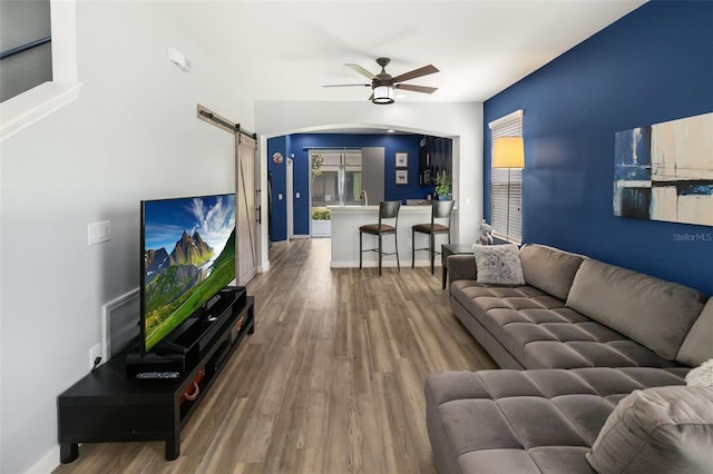 living room with ceiling fan, a barn door, and wood-type flooring