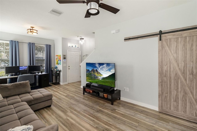 living room with ceiling fan, a barn door, and wood-type flooring