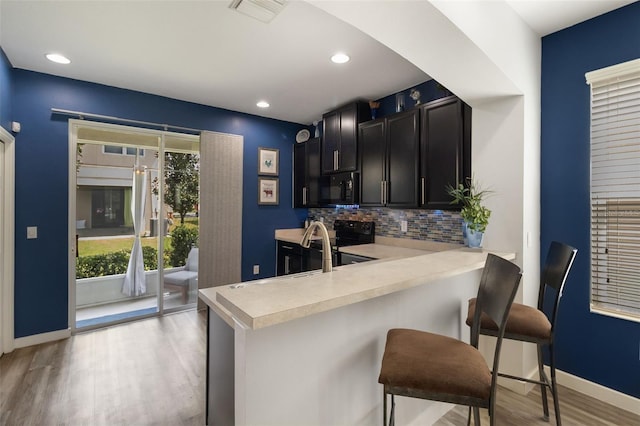 kitchen with light hardwood / wood-style floors, black appliances, a kitchen bar, and kitchen peninsula