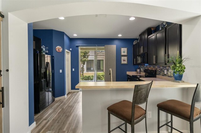 kitchen featuring black appliances, kitchen peninsula, tasteful backsplash, and a breakfast bar