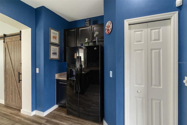 kitchen featuring a barn door, black refrigerator with ice dispenser, and dark hardwood / wood-style floors