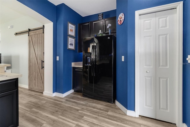 kitchen featuring a barn door, light hardwood / wood-style floors, and black fridge