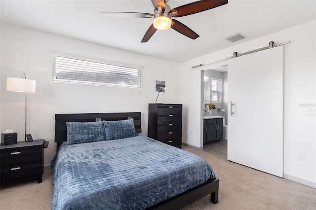 carpeted bedroom featuring ensuite bath, multiple windows, ceiling fan, and a barn door