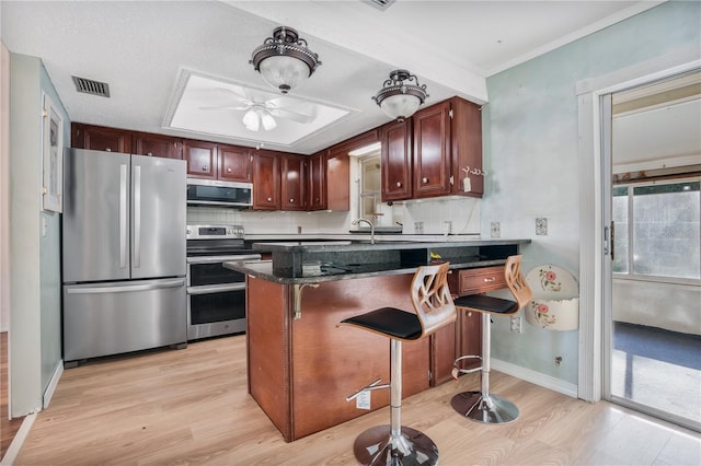 kitchen with appliances with stainless steel finishes, a kitchen breakfast bar, light hardwood / wood-style floors, tasteful backsplash, and ceiling fan