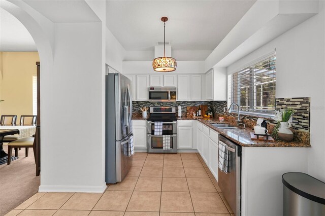 kitchen with pendant lighting, dark stone counters, white cabinets, sink, and appliances with stainless steel finishes