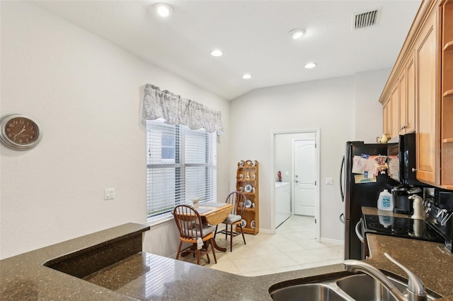 kitchen featuring light tile patterned floors, black appliances, sink, vaulted ceiling, and washer and clothes dryer