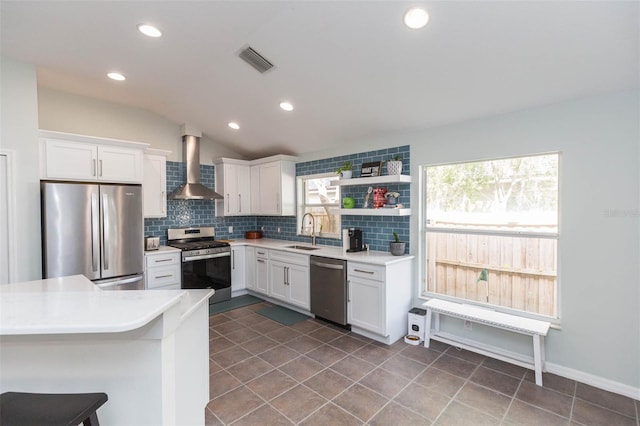 kitchen featuring sink, vaulted ceiling, wall chimney exhaust hood, appliances with stainless steel finishes, and white cabinetry