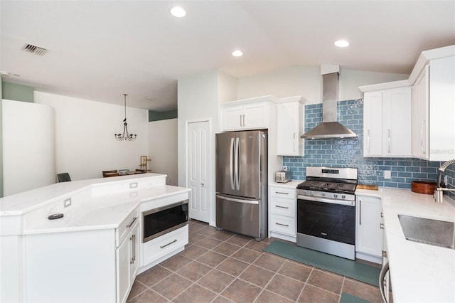 kitchen featuring white cabinets, pendant lighting, wall chimney range hood, and appliances with stainless steel finishes