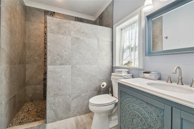 bathroom featuring a tile shower, hardwood / wood-style floors, ornamental molding, vanity, and toilet