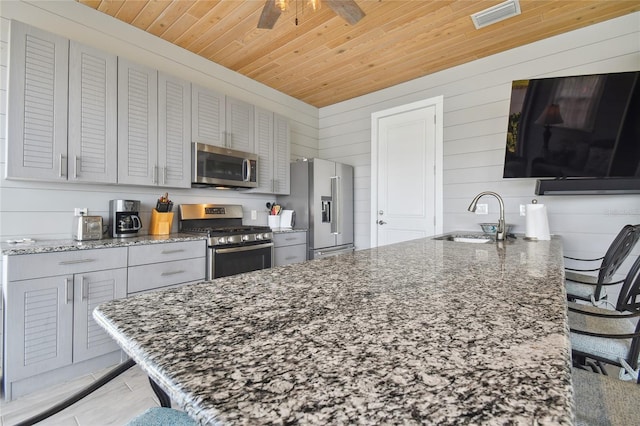 kitchen with appliances with stainless steel finishes, wood walls, sink, and a breakfast bar