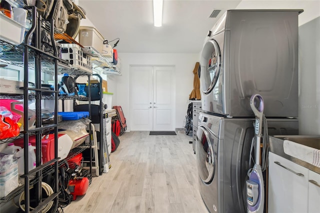 clothes washing area featuring stacked washer / drying machine and light hardwood / wood-style flooring