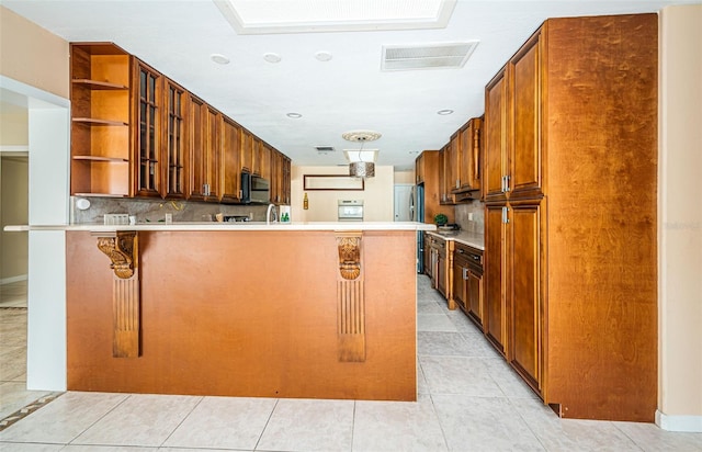 kitchen with light tile patterned floors, kitchen peninsula, backsplash, appliances with stainless steel finishes, and a kitchen bar