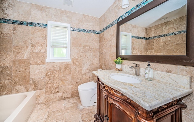 bathroom with tile walls, a tub, vanity, and toilet