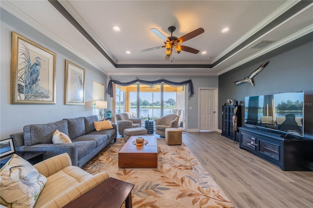 living room featuring a raised ceiling, crown molding, and light hardwood / wood-style floors