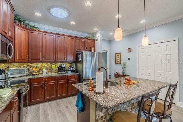 kitchen with decorative light fixtures, a center island with sink, appliances with stainless steel finishes, crown molding, and light hardwood / wood-style floors