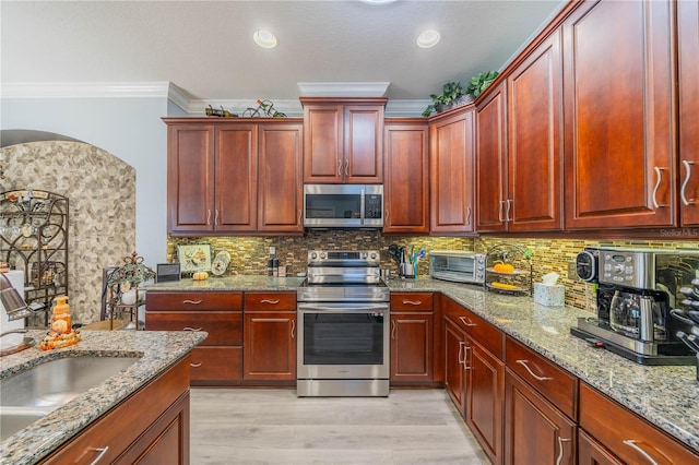 kitchen with appliances with stainless steel finishes, light hardwood / wood-style floors, tasteful backsplash, light stone countertops, and ornamental molding