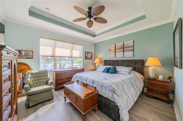 bedroom with ceiling fan, a raised ceiling, crown molding, and light hardwood / wood-style flooring