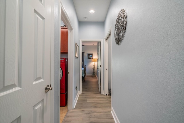 corridor with light hardwood / wood-style floors and washer / dryer