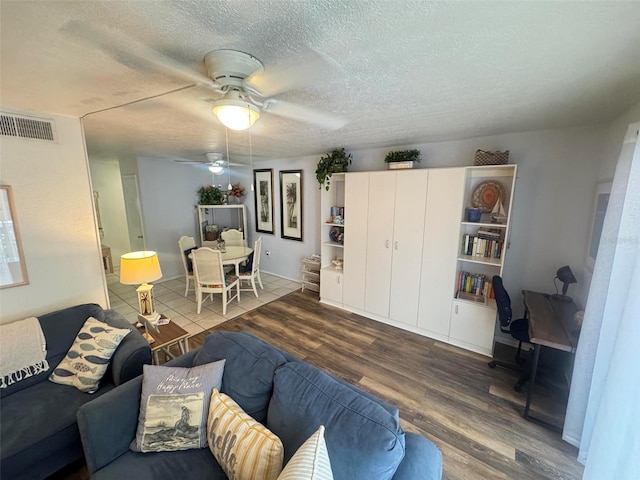 living room featuring a ceiling fan, wood finished floors, visible vents, and a textured ceiling