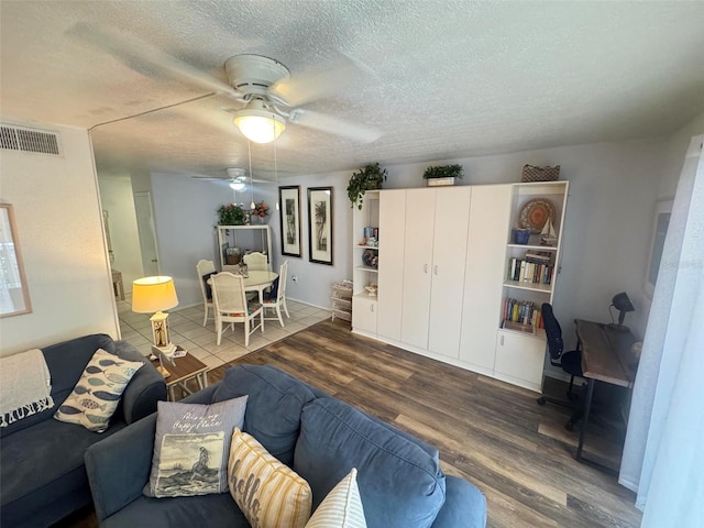 living area with visible vents, a ceiling fan, a textured ceiling, and wood finished floors