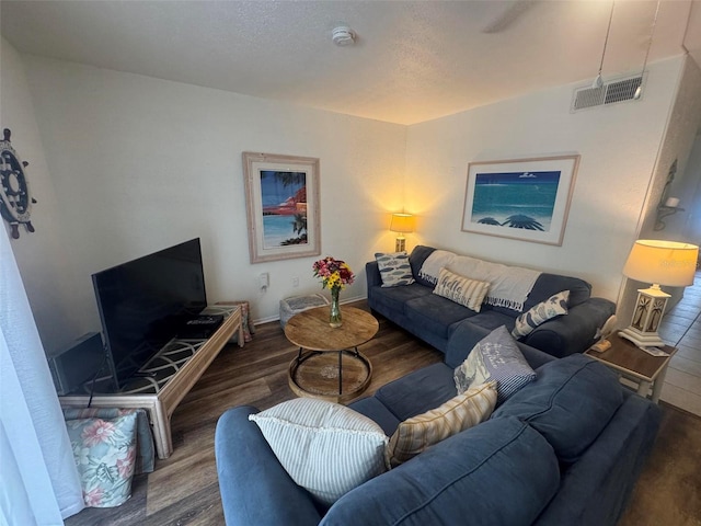 living room featuring visible vents, a textured ceiling, baseboards, and wood finished floors