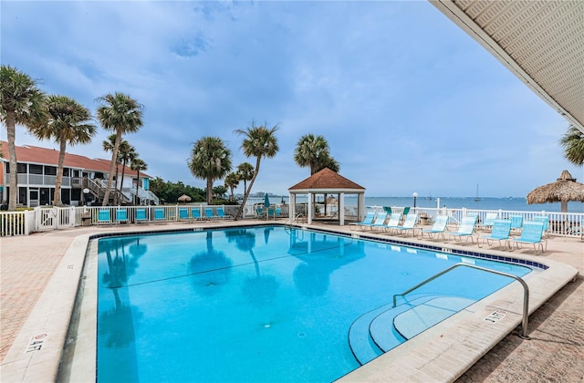 pool with a gazebo, a water view, and fence