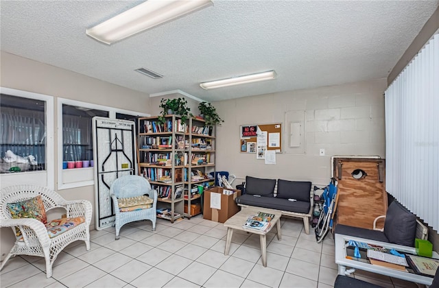 sitting room featuring concrete block wall, light tile patterned flooring, visible vents, and a textured ceiling