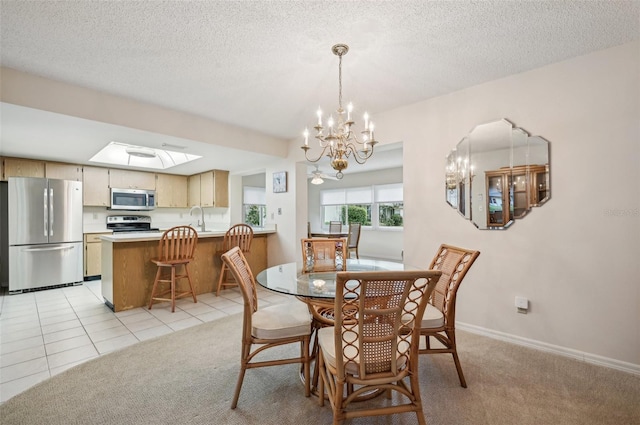 dining space featuring light carpet, sink, a chandelier, a textured ceiling, and a skylight