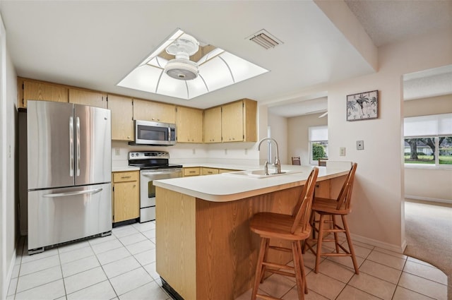 kitchen featuring light brown cabinetry, kitchen peninsula, ceiling fan, stainless steel appliances, and light tile patterned floors