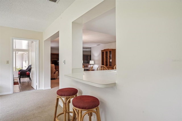 kitchen with a kitchen bar, carpet, kitchen peninsula, and a textured ceiling