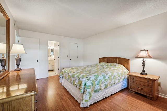 bedroom featuring a textured ceiling, ensuite bath, and hardwood / wood-style flooring