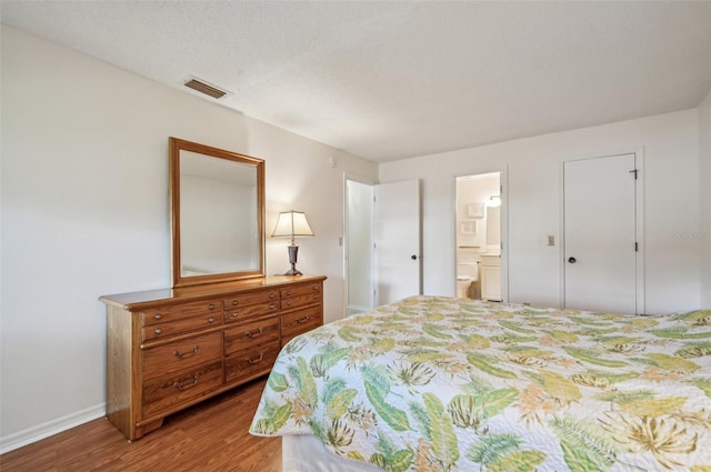 bedroom with connected bathroom, a textured ceiling, and hardwood / wood-style flooring