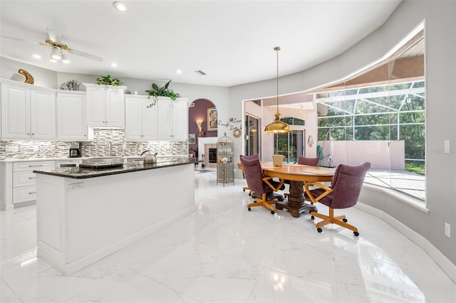 kitchen featuring white cabinetry, a center island, ceiling fan, backsplash, and pendant lighting