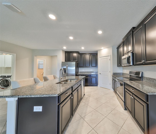 kitchen featuring a kitchen island with sink, a breakfast bar area, appliances with stainless steel finishes, washer / dryer, and sink